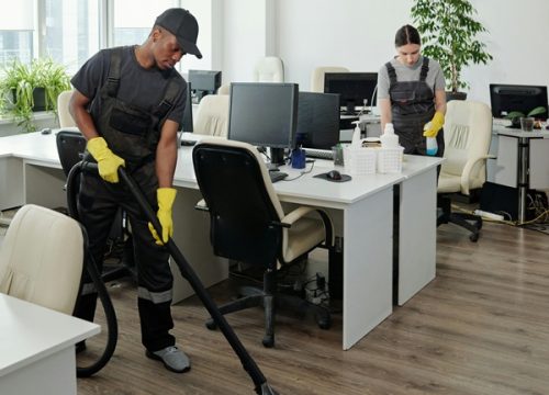 two young cleaning service workers vacuum and clean office desks floor